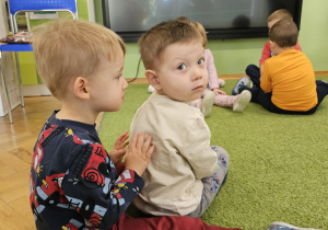 Dwóch chłopców masuje plecy. Jeden z nich ma beżową bluzę a drugi z motywem traktorów.