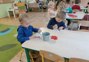 Dwóch chłopców siedzi przy stoliku i przykleja kartki papieru na szablon jabłka.