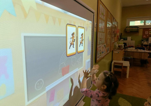 Dziewczynka stoi przed ekranem. Na ekranie widać dwie pary z kotem w butach.