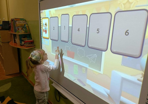 Dziewczynka w kitce i różowej bluzce dotyka ekranu.