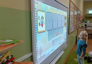 Dziewczynka w niebieskiej bluzce patrzy na ekran, na którym widać Pinokio.