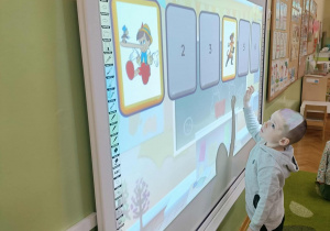 Chłopiec w szarej bluzie dotyka ekranu.