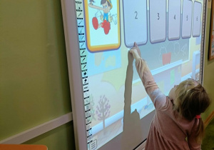 Dziewczynka w różowej sukience dotyka ekranu.