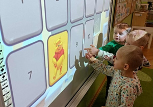 Trzech chłopców stoi przy ekranie. Na ekranie widać Kubusia Puchatka.