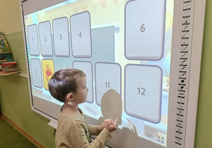 Chłopiec w beżowej bluzce dotyka ekranu.