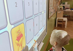 Chłopiec w szaro-czerwonej bluzie dotyka ekranu. Na ekranie widać Kubusia Puchatka.