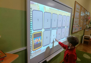 Chłopiec w czerwonej bluzie dotyka karty z cyfrą "9"