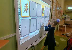 Dziewczynka w granatowej sukience dotyka ekranu.