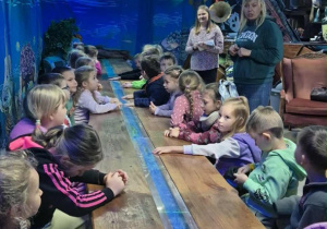 Dzieci siedzą przy drewnianym stole. Wokół widać niebieską dekorację.