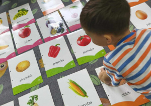 Na dywanie leżą plansze z jedzeniem. Dzieci siedzą wokół.