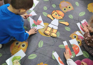 Dzieci układają puzzle na dywanie. Po środku leży szablon człowieka.