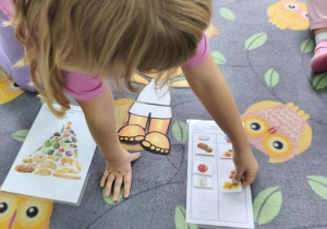 Dziewczynka segreguje jedzenie na zdrowe i nie zdrowe. Obok leży fotografia z piramidą zdrowia.