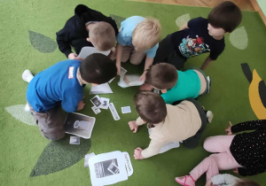 Dzieci siedzą na dywanie i dopasowywują karty do siebie.