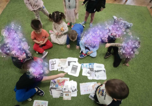 Dzieci siedzą na dywanie i dopasowywują karty do siebie.