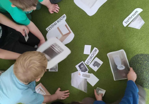 Dzieci siedzą na dywanie i dopasowywują karty do siebie.