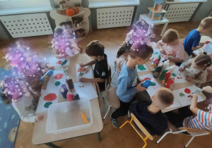 Dzieci siedzą przy stolikach i malują farbami.