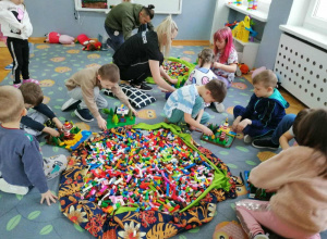 Dzieci budują z klocków LEGO. Na środku leży duży worek z klockami.