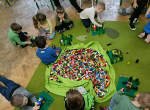 Dzieci budują z klocków LEGO. Na środku leży duży worek z klockami.