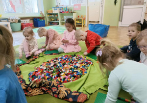 Dzieci siedzą wokół worka na zielonym dywanie.