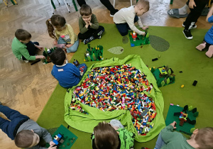Dzieci budują z klocków LEGO. Na środku leży duży worek z klockami.