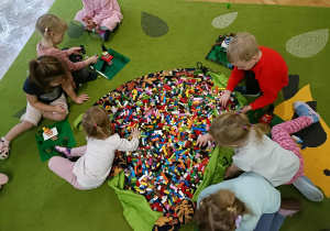 Siódemka dzieci siedzi wokół worka i buduje z klocków.