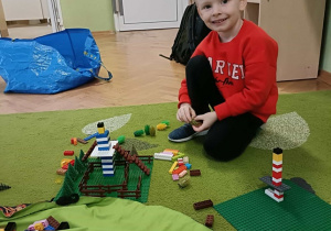 Chłopiec buduje z klocków i uśmiecha się do zdjęcia.