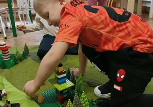 Chłopiec w pomarańczowej koszulce buduje z klocków.