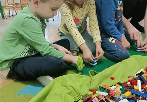 Trójka dzieci siedzi na dywanie i buduje z klocków.