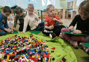 Piątka dzieci siedzi na dywanie i buduje z klocków.