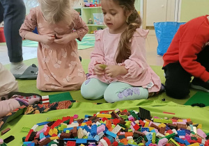 Dwie dziewczynki siedzą na dywanie i budują z klocków.