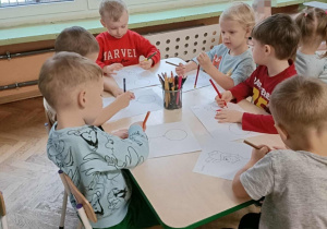 Szóstka dzieci siedzi przy stoliku i koloruje kolorowanki z misiem.