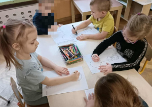 Piątka dzieci siedzi przy stoliku i koloruje kolorowanki z misiem.