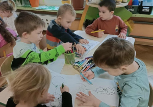 Piątka dzieci siedzi przy stoliku i koloruje kolorowanki z misiem.