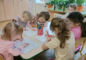 Szóstka dzieci siedzi przy stoliku i koloruje kolorowanki z misiem.