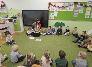 Dzieci i Pani Pedagog siedzą w kole na zielonym dywanie.