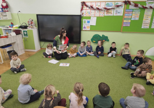 Dzieci i Pani Pedagog siedzą w kole na zielonym dywanie.