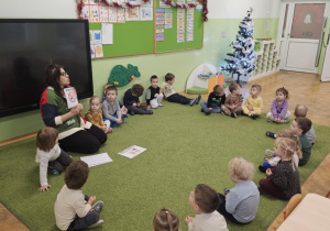 Dzieci i Pani Pedagog siedzą w kole na zielonym dywanie.