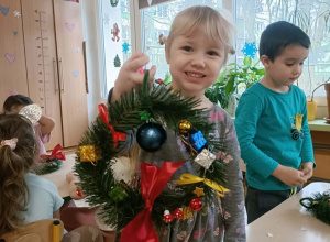 Dziewczynka w szarej sukience trzyma w dłoni skończony wianek.