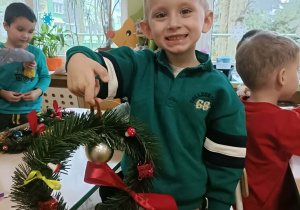 Chłopiec w turkusowej bluzie trzyma w dłoni skończony wianek.