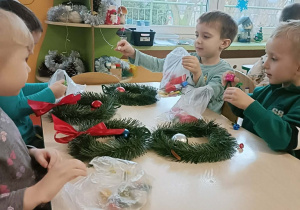 Czwórka dzieci siedzi przy stole i wykonuje wianki.