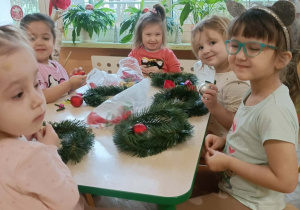 Pięć dziewczynek siedzi przy stole i wykonuje wianki.