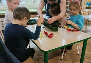 Czwórka dzieci siedzi przy stole i wykonuje wianki.
