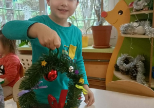 Chłopiec w turkusowej bluzie trzyma w dłoni skończony wianek.