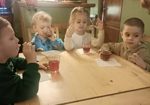 Czwórka dzieci siedzi przy stoliku, je ciasteczko i pije sok.