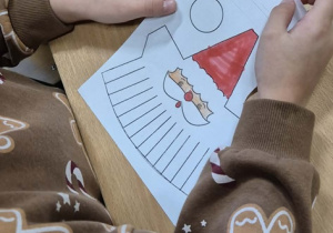 Dziecko w bluzie w pierniczki koloruje Mikołaja.