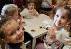 Piątka dzieci siedzi przy stoliku i je ciasteczka.