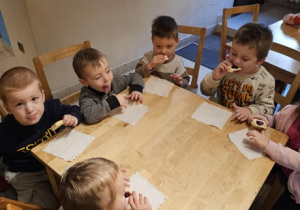 Piątka dzieci siedzi przy stoliku i je ciasteczka.