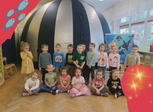 Dzieci stoją na tle kopuły. Po prawej stronie stoi reklama. Na oknie w sali naklejony jest Św.Mikołaj.