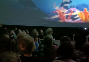 Dzieci siedzą w kopule i oglądają pokaz o rafie koralowej.