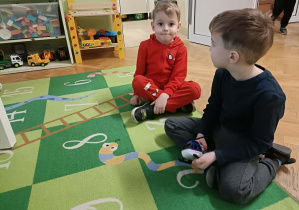 Dwóch chłopców siedzi na zielonym dywanie w cyferki.